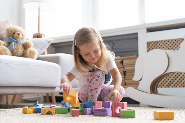 自宅のプレイルームでブロックおもちゃを遊んでいる小さなかわいい女の子。