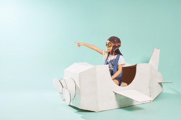 Little cute girl playing with a cardboard airplane White retro style cardboard airplane on mint green background Childhood dream imagination concept