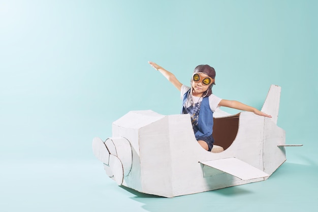 Little cute girl playing with a cardboard airplane White retro style cardboard airplane on mint green background Childhood dream imagination concept