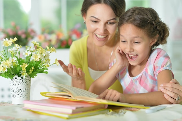 Маленькая милая девочка читает книгу с мамой за столом дома