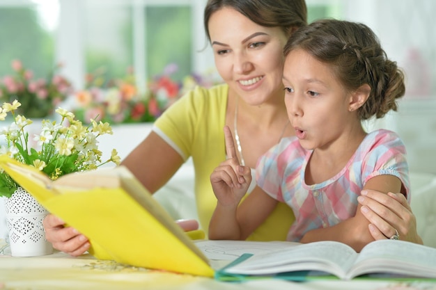 Little cute girl reading book with mother at the table at home