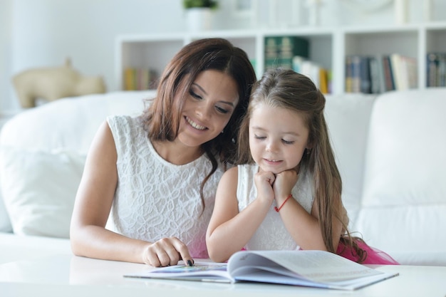 Little cute girl reading book with mother at the table