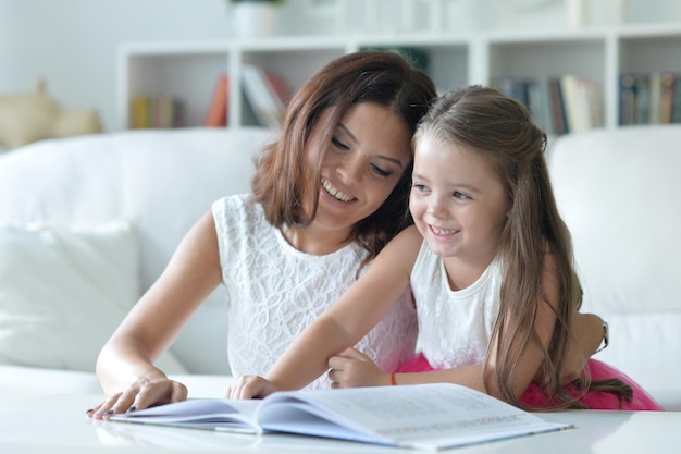 Little cute girl reading book with mother at the table