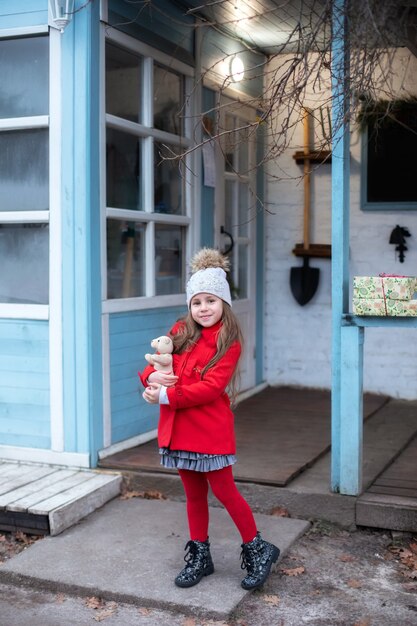 赤いコートを着た小さなかわいい女の子がクリスマスプレゼントを持って歩いています