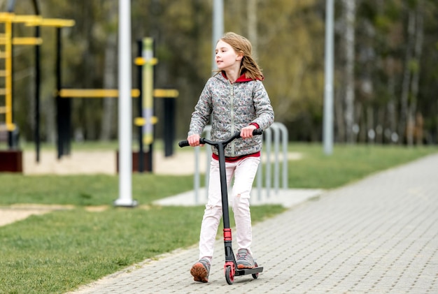 Little cute girl riding a scooter on a path in the park