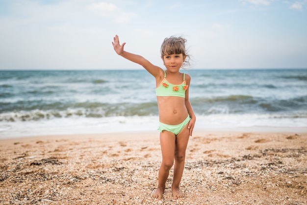 暖かい夏の日の週末に海で泳いでいる間、小さなかわいい女の子が親指を立てます。休暇中の幸せな子供たちの概念。コピースペース