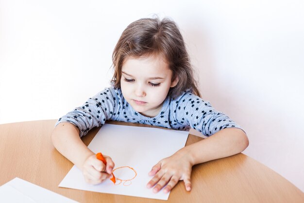 Una bambina piccola e carina si siede a un tavolo e disegna