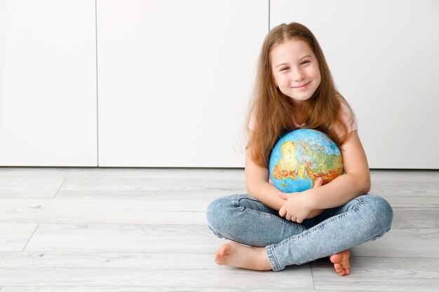 写真 地球を抱きしめて床に座っている可愛い小さな女の子