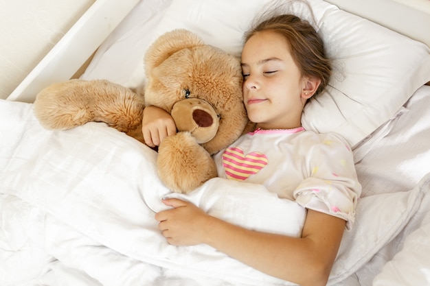 Little cute girl sleeping and hugging big teddy bear at bed