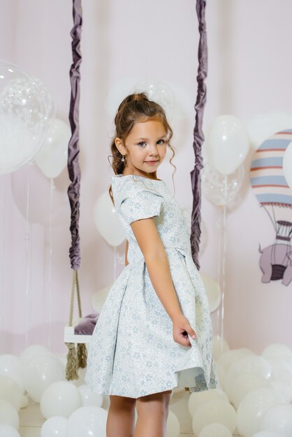 A little cute girl smiles and poses against the background of a swing with balloons.