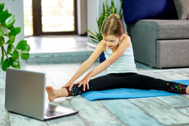 Little cute girl in sportswear on blue mat practicing gymnastics at home