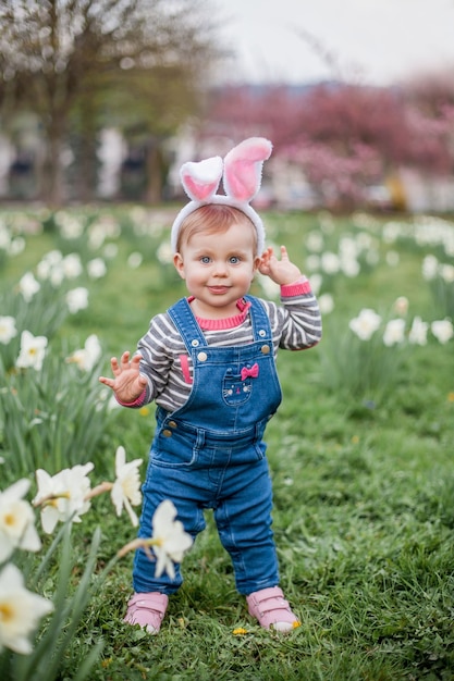 Little cute girl standing on the grass near the daffodils