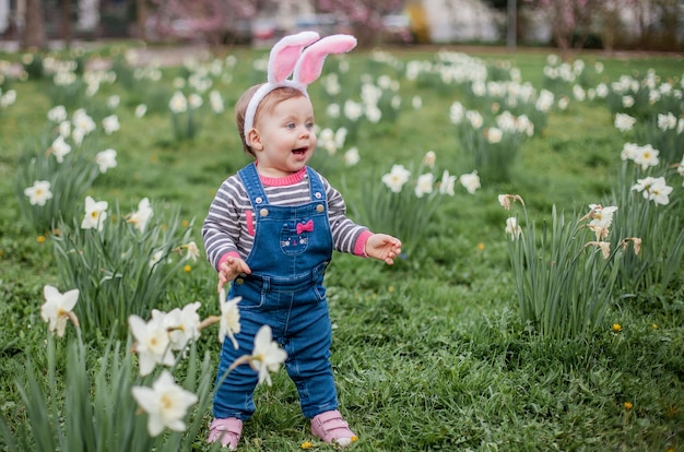 Little cute girl standing on the grass near the daffodils