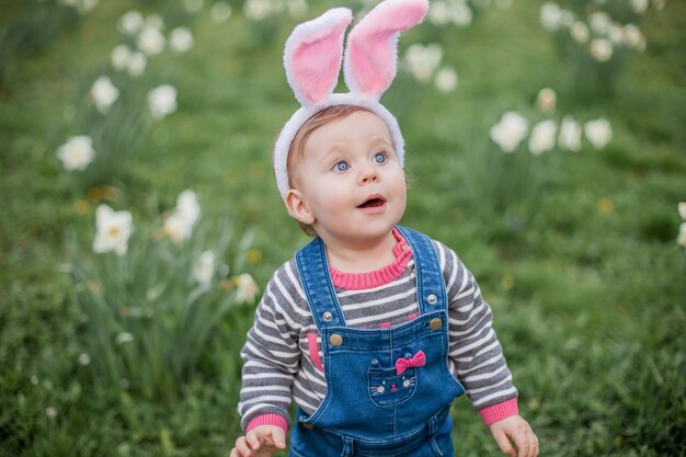 Little cute girl standing on the grass near the daffodils