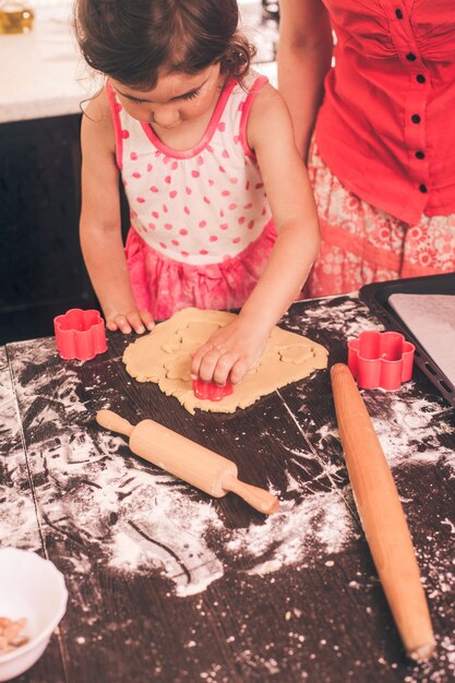 Little cute girl stretching the dough in the kitchen