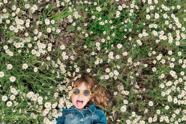 Little cute girl in sunglasses lies on the field with daisies.