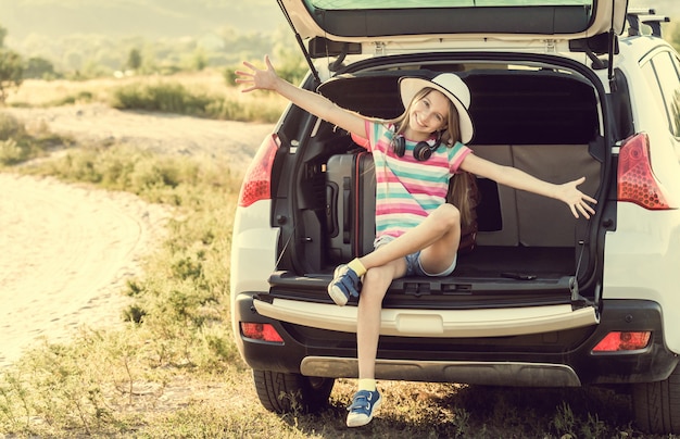Маленькая милая девушка в багажнике машины с чемоданами
