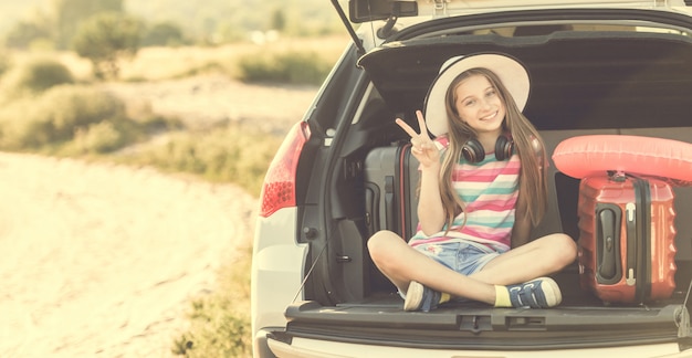 Little cute girl in the trunk of a car with suitcases