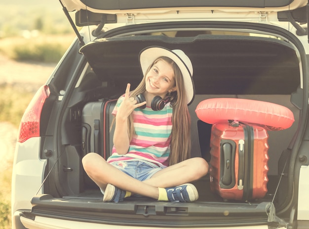 Bambina carina nel bagagliaio di un'auto con valigie