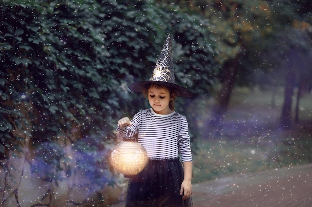 Little cute girl in witch costume holding paper lantern Kid having fun on Halloween holiday