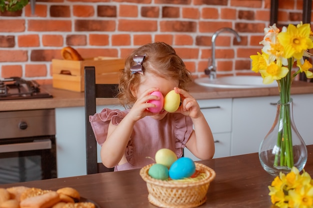 Little cute girl with a basket of Easter eggs in the kitchen at home