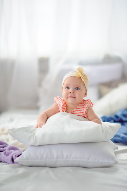 Little cute girl with big blue eyes. Girl trying to climb over pillows