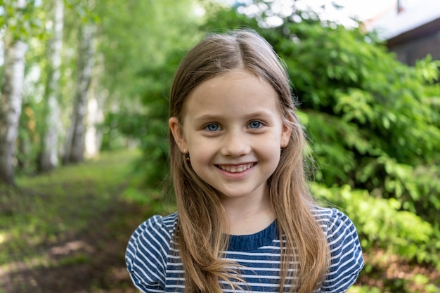 A little cute girl with blonde hair smiles at the camera closeup shooting vacation in the forest in