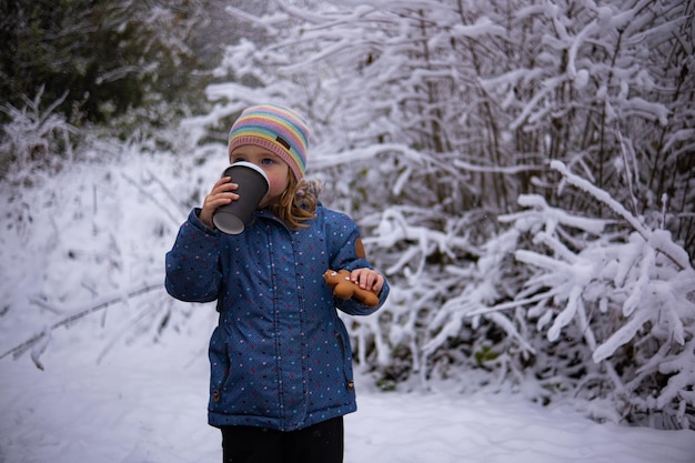 Little cute girl with a cup of tea and a gingerbread man on a snowy winter day