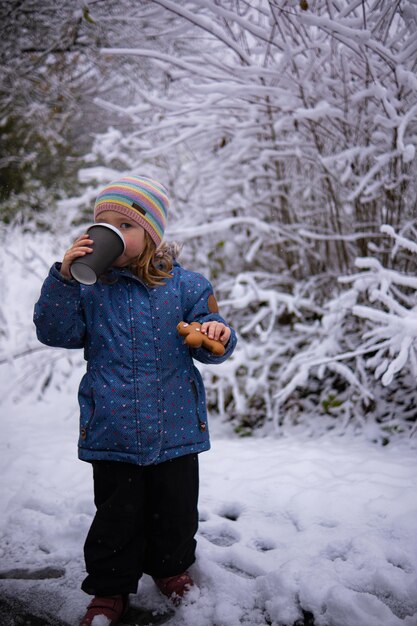 눈 내리는 겨울날 차 한 잔과 진저브레드 맨을 들고 있는 귀여운 소녀