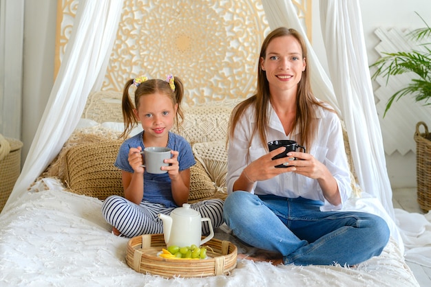 彼女のお母さんと一緒に小さなかわいい女の子は寝室の家族の朝食でお茶を飲んでいます