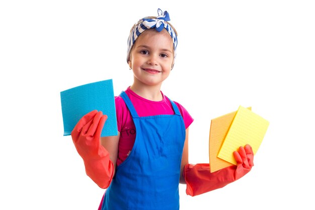 Little cute girl with ponytail in pink shirt and blue apron with red gloves holding colored dusters