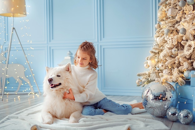 Little cute girl with a white malamute dog near christmas tree.