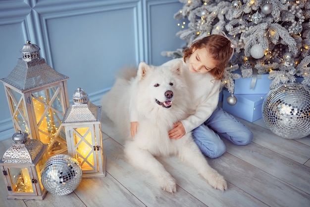 Little cute girl with a white malamute dog near christmas tree.