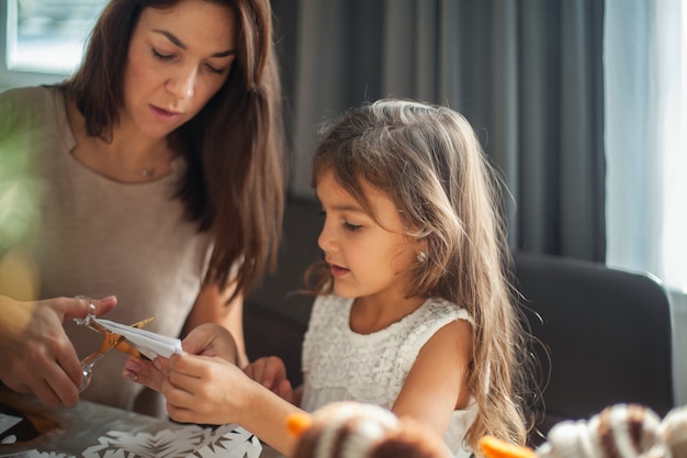 Little cute girl and young beautiful woman cut snowflakes from white paper. Gingerbread and cocoa with marshmallows. The concept of preparation for the New Year and Christmas.