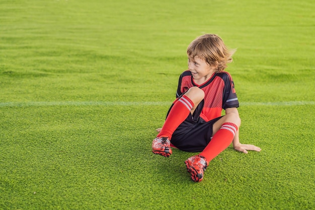 Little cute kid boy in red football uniform playing soccer football on field outdoors Active child making sports with kids or father Smiling happy boy having fun in summer