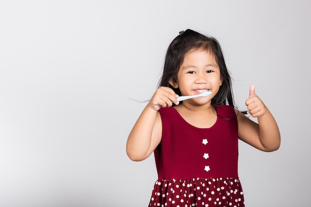 Little cute kid girl smile brushing teeth and show thumb up finger for good sign