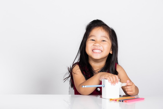 숙제를 하는 동안 연필 깎이를 사용하여 작은 귀여운 꼬마 소녀 미소