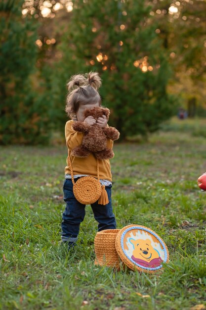 Little cute sad girl holding in hands brown teddy bear, upset child spending time outdoors in spring time