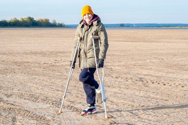 Little cute smiling girl in a warm jacket on crutches on a sunny spring day