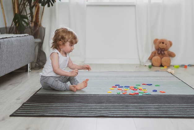 Little cute toddler playing with toy letters sitting on the floor