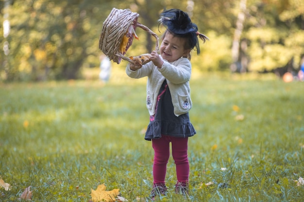 秋の公園で葉のバスケットで遊んでいる小さなかわいい魔女。