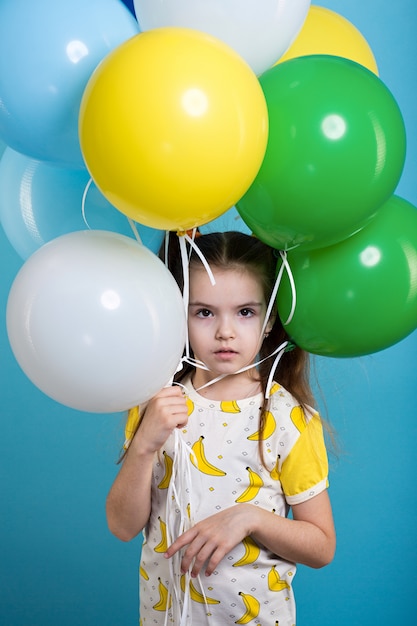 Фото Маленькая темноволосая девушка с разноцветными шариками на синем фоне