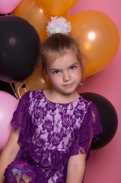 Little dark haired girl with colourful balloons on pink background