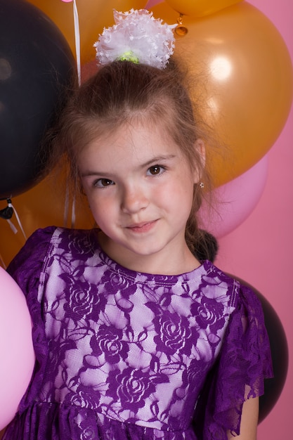 Little dark haired meisje met kleurrijke ballonnen op roze achtergrond