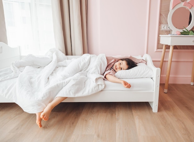 A little darkhaired girl lying barefoot in bed the child woke up after sleeping good morning