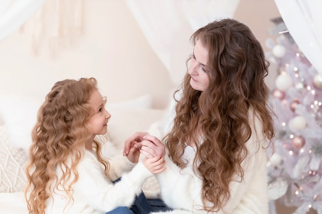 Little daughter hugging mother for christmas. girl and woman waiting new year in home at badroom.