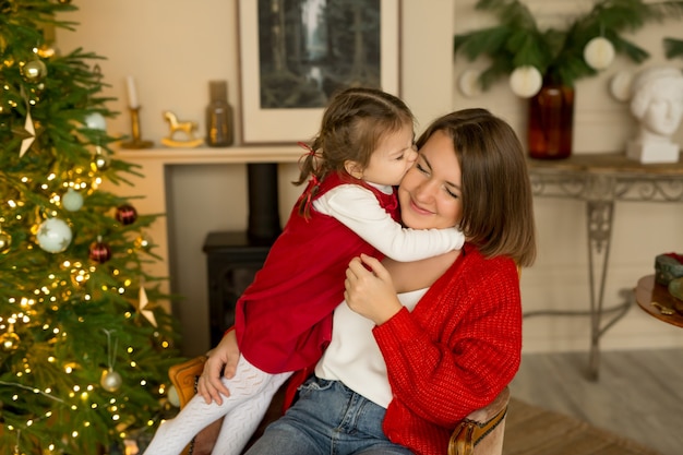 A little daughter kisses and hugs her mom on Christmas Eve