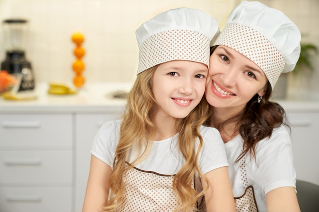 Little daughter and mother in aprons looking at camera.