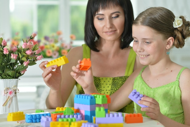 Little daughter and mother playing with colorful plastic blocks at home