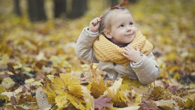 Little daughter plays with yellow leaves in autumn park - the girl is happy and laughing